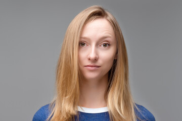 Fototapeta premium Close up Portrait of young beautiful woman with blond hair and in blue T shirt look at camera, posing in studio, isolated on grey studio background