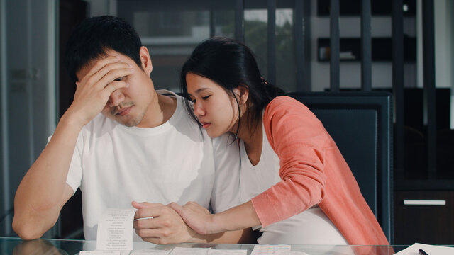 Young Asian Pregnant couple records of income and expenses at home. Dad worried, serious, stress while record budget, tax, financial document working in living room at home concept. - Powered by Adobe