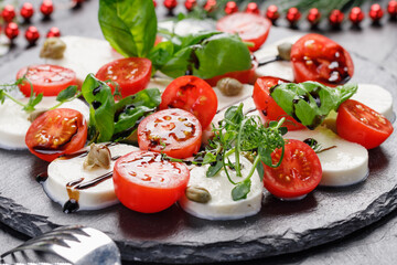 traditional caprese salad on a dark plate. Tomatoes with mozzarella cheese with basil on a dark background.