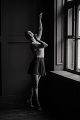 Ballerina in dark bodysuit, in dress in dark interior Studio. Wall of bricks, piano.