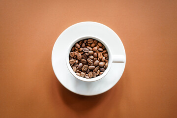 Obraz premium Top view of roasted coffee beans in white coffee cup with brown background 