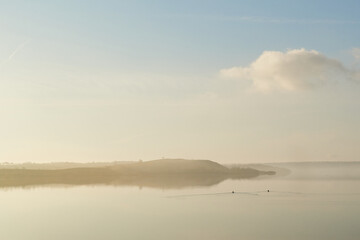 mist laying over the calm water on a silent morning at Flyndersoe lake in Denmark