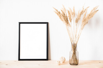 Dried flowers and a photoframe against a light wall in a minimalist style.