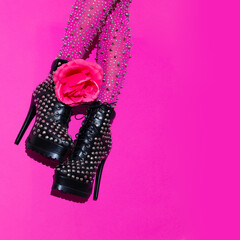 Fashion legs and roses in heel black boots on pink  minimal background. Stylish accessories shoes...