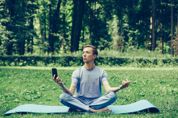 Young attractive white man learns to meditate in the park in front of smartphone