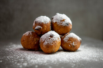 Yummy homemade small Dutch oil balls delicacy with sugar powder traditionally eaten on New Year's Eve in The Netherlands. Studio low key food closeup still life against a gray background.