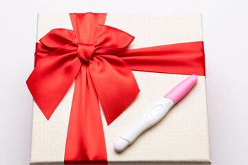 Pregnancy test with a positive result in the form of the heart. Lies on the box with a red bow. On white isolated background.