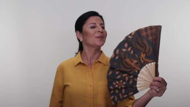 Tired, overheated middle-aged lady is cooling off with a fan. Tired, overheated middle-aged woman, suffering from menopause fatigue,complaining of heat at home, uncomfortable weather problem in summer