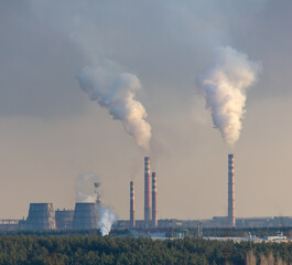 Smoke from chimneys at the plant in the rays of the sunset as a background.