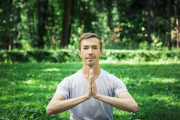 Naklejka na ściany i meble Young attractive man in sport clothes is meditating cupped in a meditation or prayer gesture with a pacified face.
