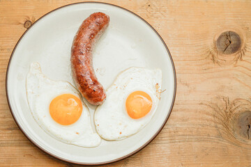 2 fried eggs and a sausage, on a wooden board