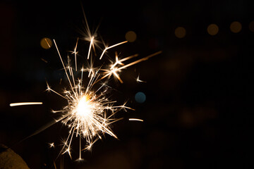 Obraz premium Bengal fire sparkles against the background of city lights, blurred bokeh. A lot of sparks