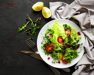 Fresh green mixed  salad bowl with tomatoes and microgreens  on black concrete background. Healthy food, top view.
