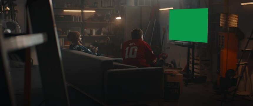 GREEN SCREEN CHROMA KEY Back view of two friends playing video game inside garage, enjoying pizza and drinks. Shot with 2x anamorphic lens