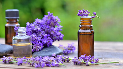 bottle of essential oil and  lavender flowers arranged on a wooden table in garden