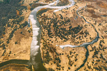 Aerial View Curved River In Early Spring Landscape. River bends Curves and dry grass landscape. Top View Of Beautiful European Nature From High Attitude. Drone View. Bird's Eye View