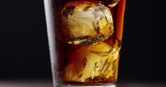 Camera goes up along the glass of cola and ice, the gas bubbles also slowly go up. Behind a dark background. Slow motion, Blackmagic Ursa Pro G2.
