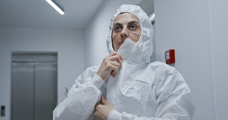 Fototapeta premium Exhausted nurse putting on hazmat PPE suit in hospital. Covid-19 coronavirus pandemic concept.