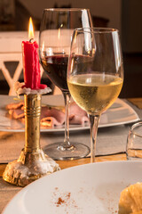 White wine glass with red wine glass on rustic trattoria table set with red candle lit in golden brass candlestick