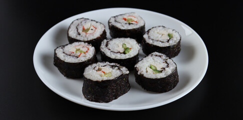 Fresh delicious sushi rolls with cucumber, crab sticks on a black background