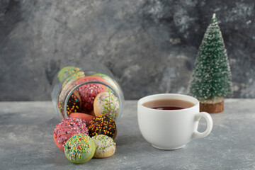 A glass jar full of small colorful doughnuts with a cup of hot tea