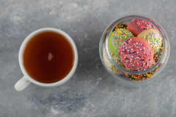 A glass jar full of small colorful doughnuts with a cup of hot tea