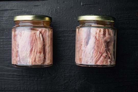 Tuna fillet in glass jar, on black wooden background, flat lay