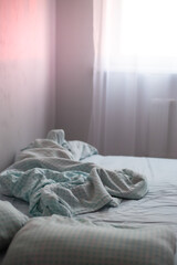 crumpled empty bed in a room at dawn. Weekend morning, loneliness. Soft focus.