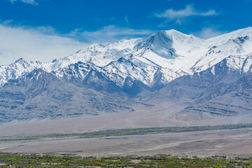 Beautiful landscape with fields of delta of Indus River, Tibetian buildings, Himalayas snow...