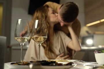 close-up two glasses on the table, a man and a woman kiss passionately on their background.