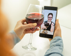 The women talk over video communication on the phone and drink red wine. The quarantined girl is not making a video call