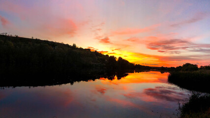 Obraz premium Very dramatic sunset scene. Colours red, orange, violet and reflections in the water. Horizontal panoramic view of a sunset