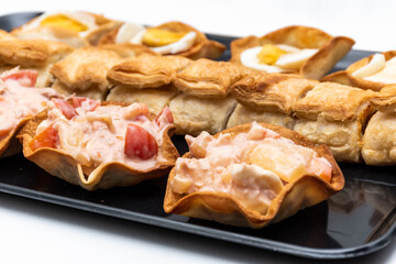 Horizontal black tray with an assortment of lids and salted canapés on a white background.