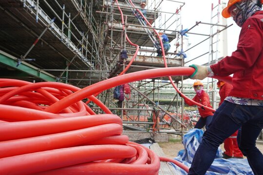 Large red power cord placed on the scaffolding floor and workers pulling high voltage cable line in chemical plants, power plants, oil & gas industry or onshore.