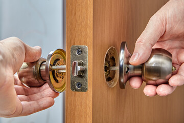 Carpenter inserts one half of the doorknob In through the latch. - obrazy, fototapety, plakaty