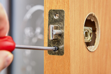 Locksmith installs door knob with lock. An Carpenter pushes standard rectangular faceplate, slide the latch into place with the bevel facing the doorjamb and secure with the two short screws.