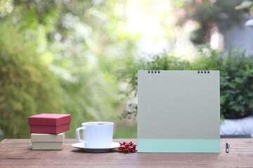 Empty calendar with white coffee cup and gift box on brown wooden table at outside
