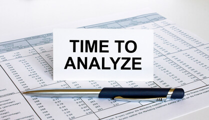 Text Time To Analyze on white card with blue metal pen on financial table