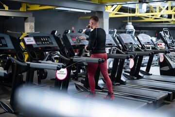 Fototapeta na wymiar The man in the gym starts running on the treadmill. Daily training.