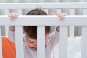 baby inside a cradle holding the bars and looking down