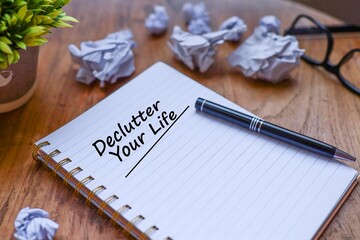 Declutter your life message written on the notebook with a pen on top, crumpled papers and eyeglasses on the wooden table 