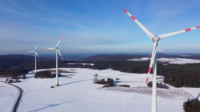 Flying towards a rotating wind turbine. Aerial view of a windfarm in a snowy winter landscape. Aerial shot of a wind farm in winter.