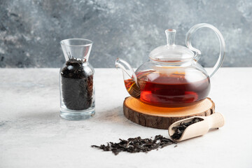A glass teapot with dried loose teas and a wooden spoon