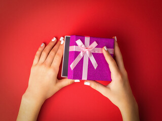 The child's hands open a gift box on a red background.