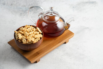 A glass teapot of tea with wooden bowl full of crackers