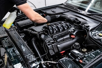 Car wash worker carefully cleaning engine with a brush