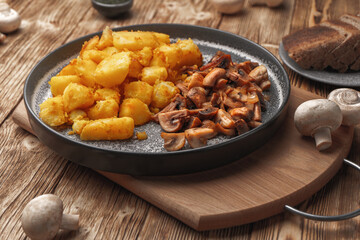 Vegetarian fried potatoes with mushrooms on a concrete plate on a wooden plank table.