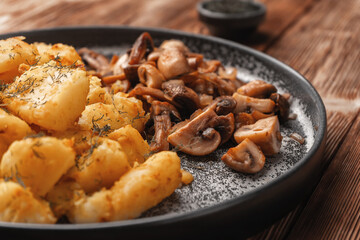 Fried mushrooms near fried potatoes decorated with greens on a concrete plate close-up