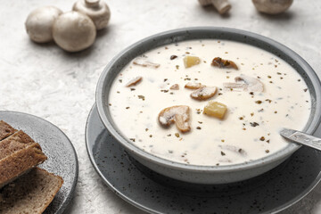 Soup with mushrooms and coconut cream in a gray plate next to raw mushrooms and a plate of bread