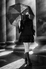 Woman in a black dress and a mask with an umbrella in her hands